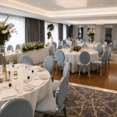 Elegant hotel ballroom with round tables, floral centrepieces, and plush chairs, perfect for weddings or events.