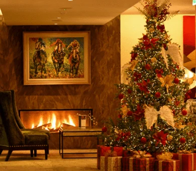 Festive hotel lobby with fireplace, cosy armchair, decorated Christmas tree, and art; welcoming holiday atmosphere.