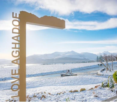 Scenic view of snow-covered mountains and lake from Aghadoe hotel grounds, featuring "LOVE AGHADOE" sign.