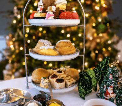 Festive afternoon tea with scones, pastries, and decorations by a Christmas tree at a hotel.