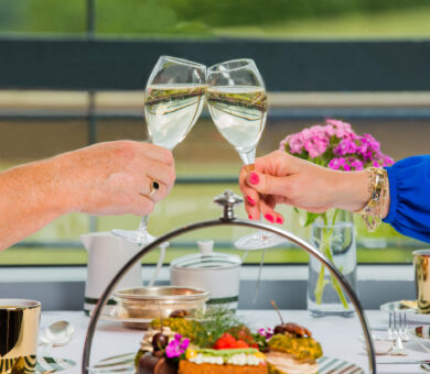 Guests toast with champagne over afternoon tea, enjoying elegant pastries and scenic views at a luxury hotel.