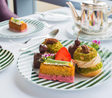 Elegant afternoon tea with assorted pastries and silver teapot on a striped plate at luxury hotel restaurant.
