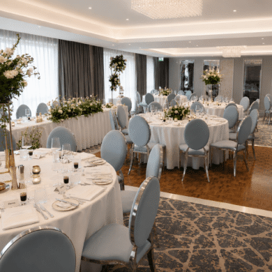 Elegant banquet room with round tables, floral centrepieces, and modern chandeliers, ideal for weddings or events.