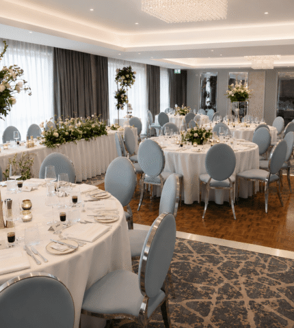 Elegant banquet room with round tables, floral centrepieces, and modern chandeliers, ideal for weddings or events.