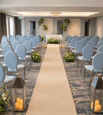 Elegant hotel event room with blue chairs, floral decor, and a carpeted aisle, perfect for weddings or conferences.