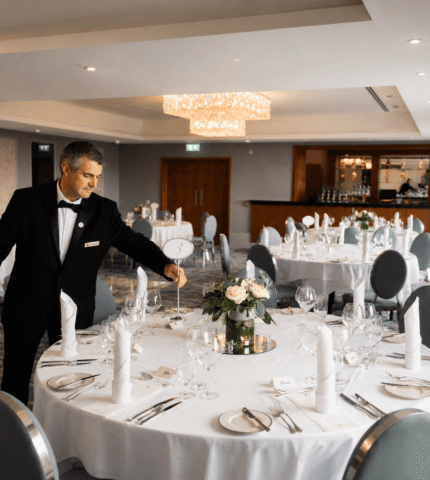 Elegant banquet hall with chandeliers, round tables set for dining, and attentive staff, ideal for weddings and events.