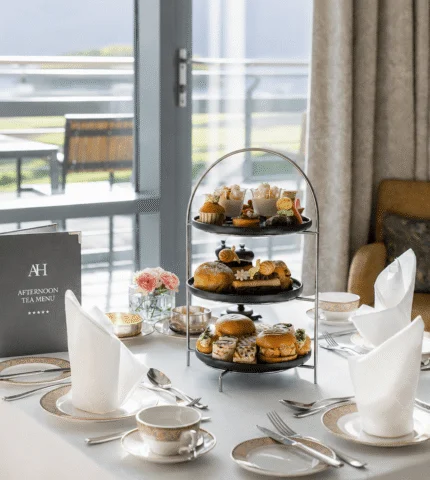 Elegant afternoon tea setup with tiered stand, scenic mountain view from hotel terrace.