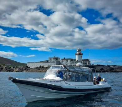 Scenic coastal view with lighthouse and guests on boat tour under blue sky at seaside hotel location.
