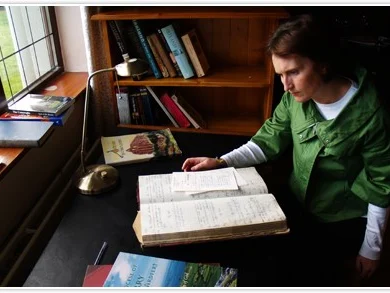 Guest reading in cosy study with natural light, wooden shelves, and a vintage desk lamp.
